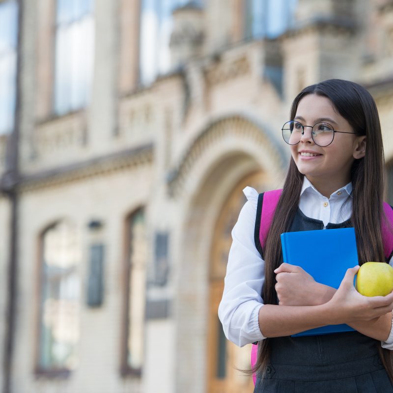 Smiling student with books and apple outside school