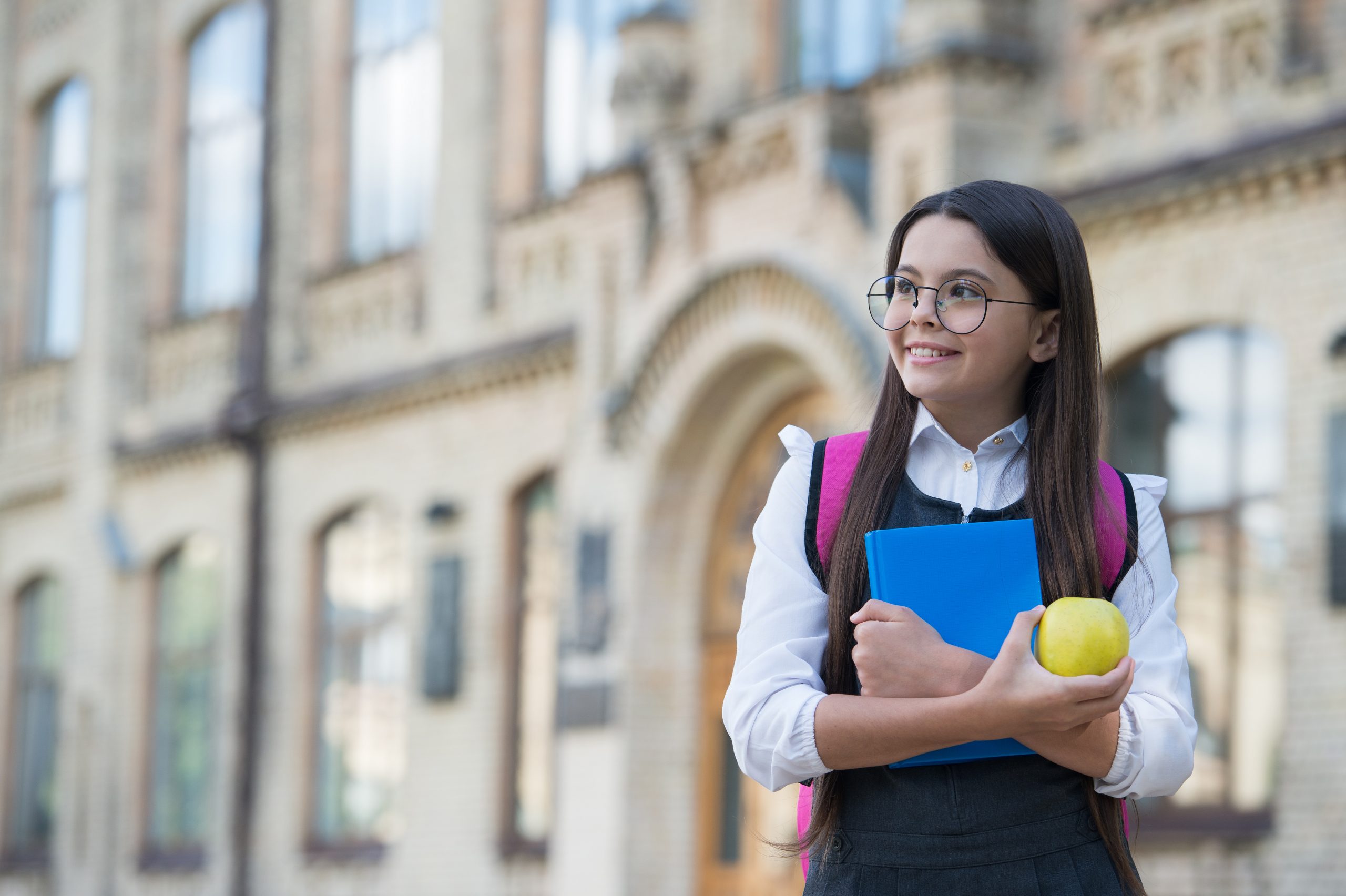 Smiling student with books and apple outside school