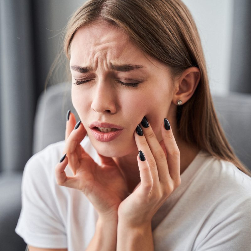 Woman touching cheeks, appears to have toothache.