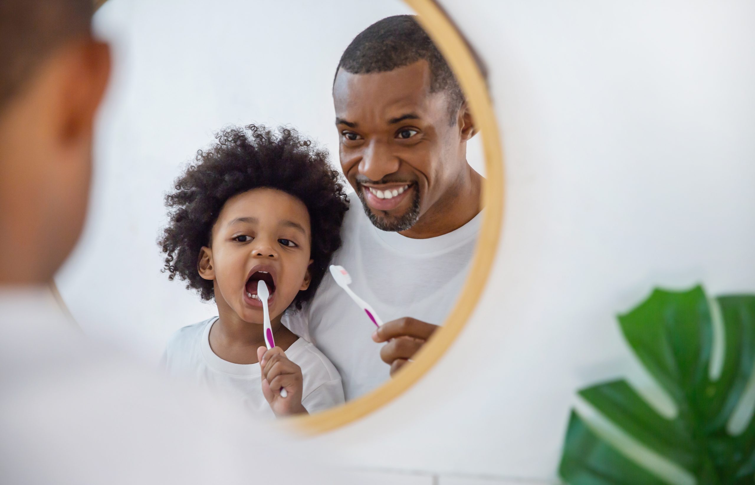 Father and child brushing teeth together in mirror