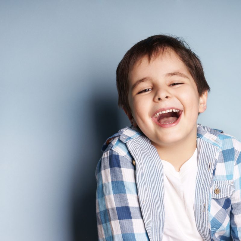 Smiling child in checkered shirt against blue background.