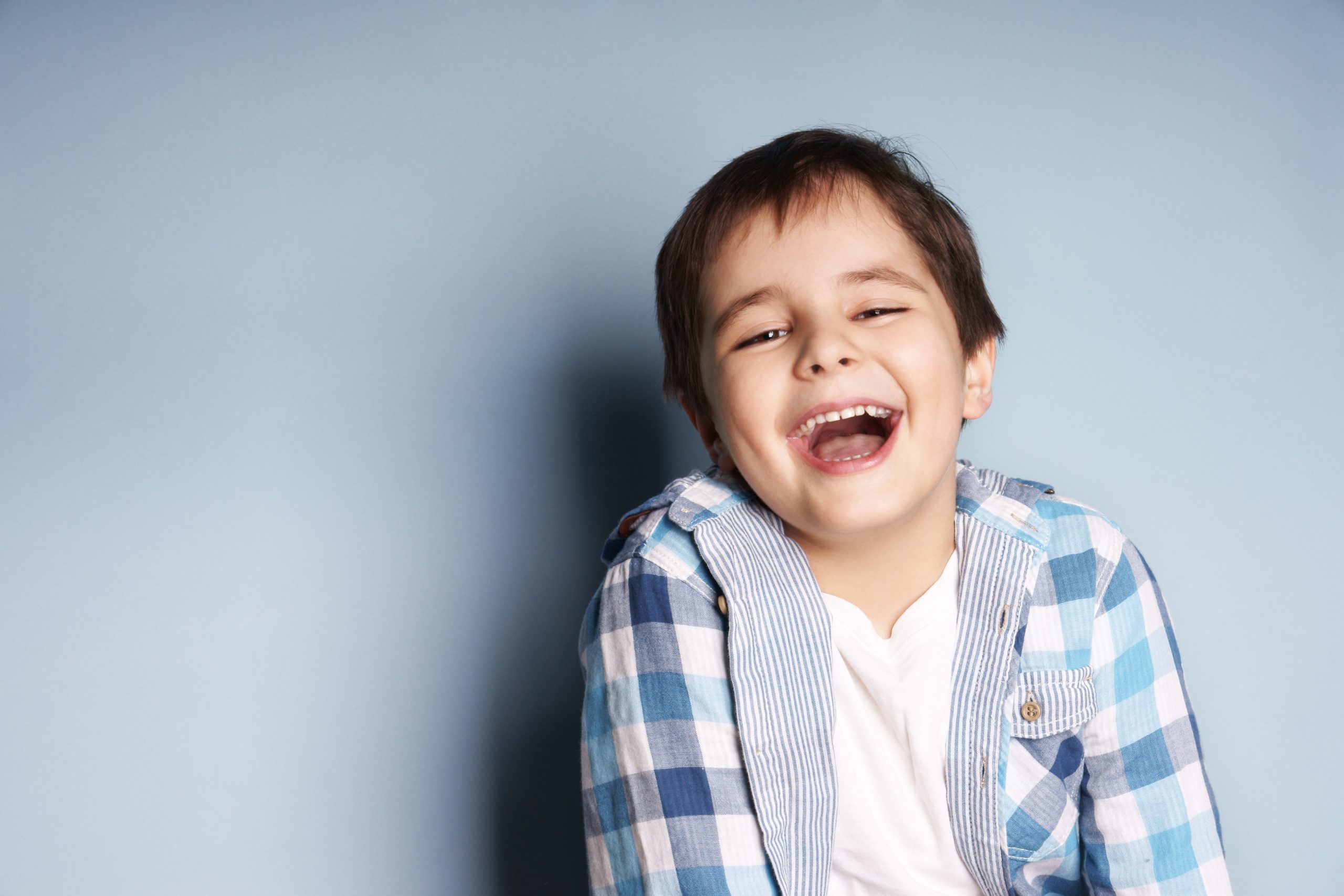 Smiling child in checkered shirt against blue background.