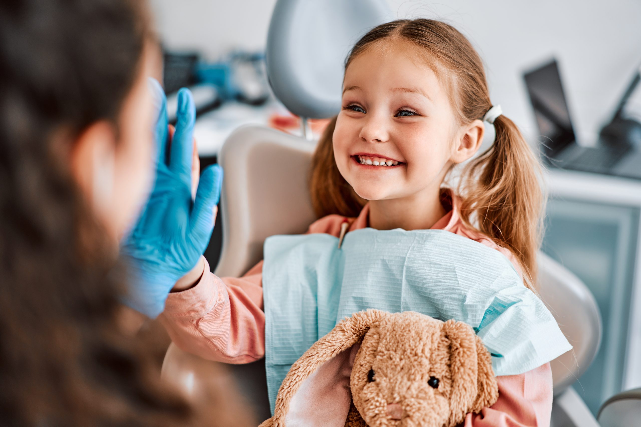 Smiling child at dentist with teddy bear and gloves.